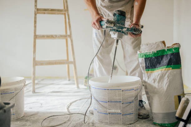 Builder's hands using manual cement mixer for mixing plastering materials and preparing it for skim coating and plastering walls in a house in renovation process. Cropped picture of man mixing plaster
